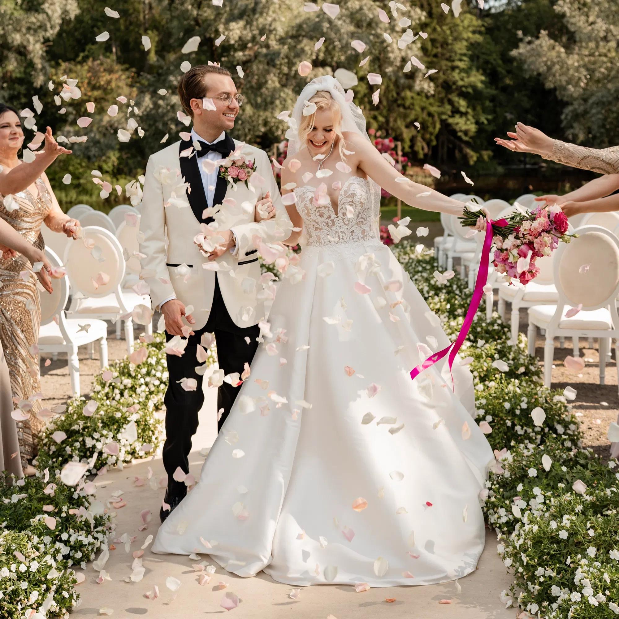 Hochzeitspaar verlässt Hand in Hand den Trauungsbereich, während Gäste Rosenblätter über sie streuen.