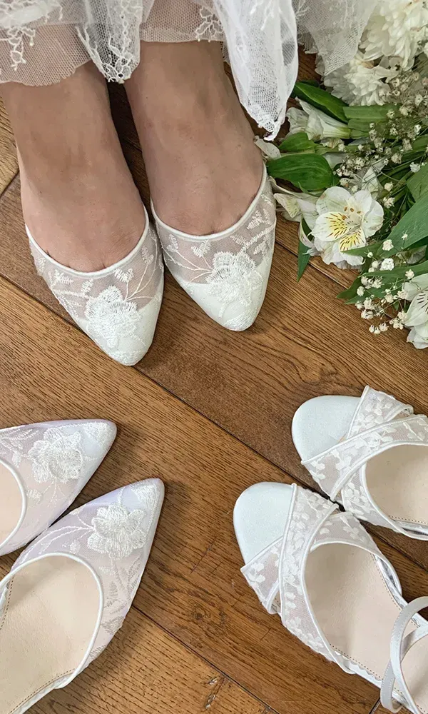 Detailaufnahme von weißen Brautsandalen mit Schleifen und floralen Accessoires – ideal für die Hochzeit