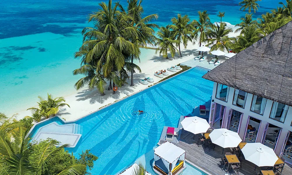 Luftaufnahme des Luxusresorts auf den Malediven mit Infinitypool, weißem Sandstrand und Palmen – perfekter Ort für eure Flitterwochen