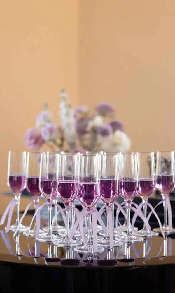 Reihe von Sektgläsern mit lila Aperitif, dekoriert mit Bändern, festlich arrangiert