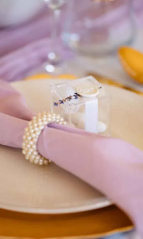 Hochzeitstisch-Dekoration mit lila Serviette, Perlenring und durchsichtigem Gastgeschenk mit Siegel