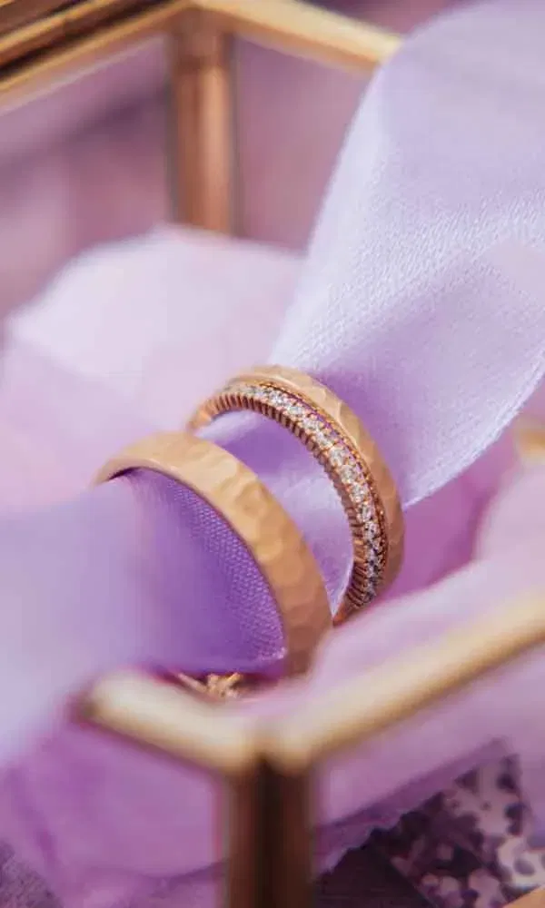 Goldene Eheringe mit Hammerschlag-Optik und Diamantbesatz auf lila Stoff präsentiert