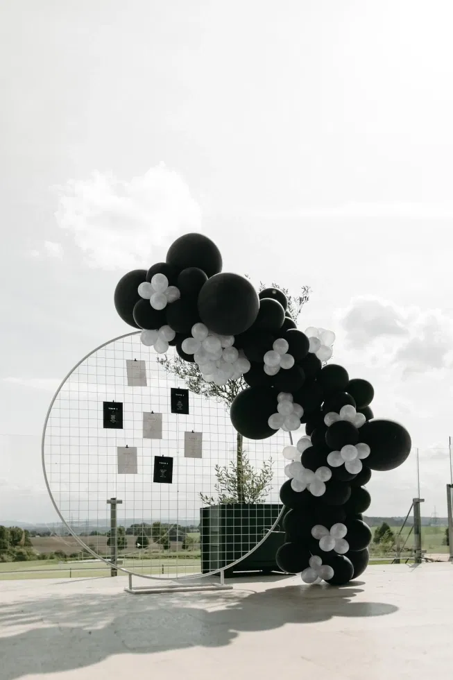 Moderner Sitzplan für eine Hochzeit mit schwarzer und weißer Ballongirlande in stilvoller Outdoor-Kulisse