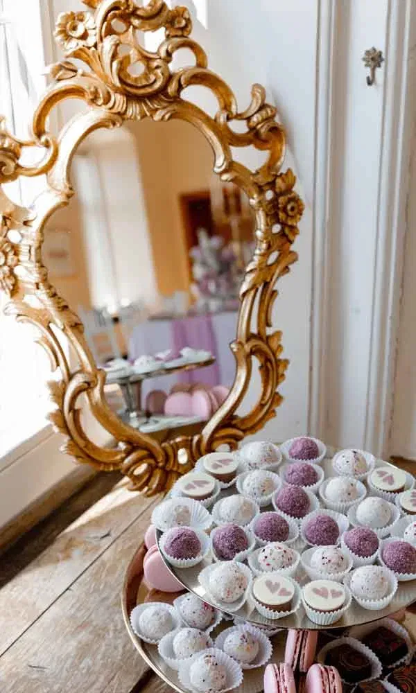 Hochzeitssüßigkeiten in Lila und Weiß auf Etagere, dekoriert mit Pralinen und Macarons vor goldenem Spiegel