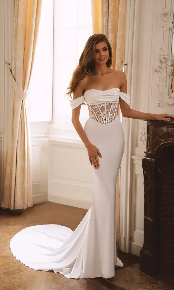 Edles Hochzeitskleid im Fit-and-Flare-Stil mit transparenter Miederoptik und langer Schleppe vor großen Fenstern.