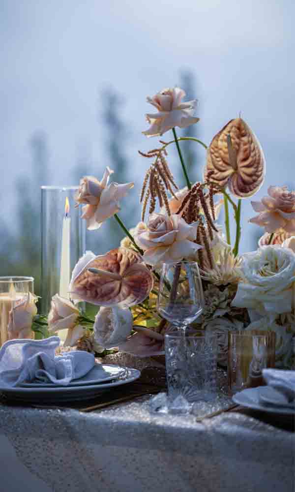 Romantische Tischdekoration mit zarten Blumenarrangements und leuchtender Kerze im Glaszylinder.