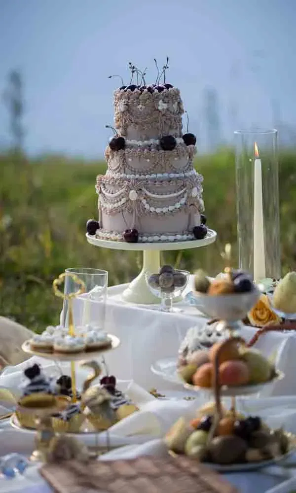 Luxus-Sweet-Table mit kunstvoller Torte, kleinen Gebäckstücken und frischem Obst im Freien.