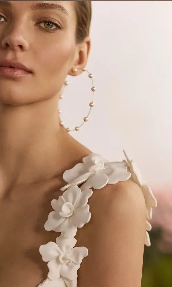 Romantisches Brautkleid-Detail: 3D-Blumenapplikationen schmücken die Träger, kombiniert mit modernem Braut-Accessoire.