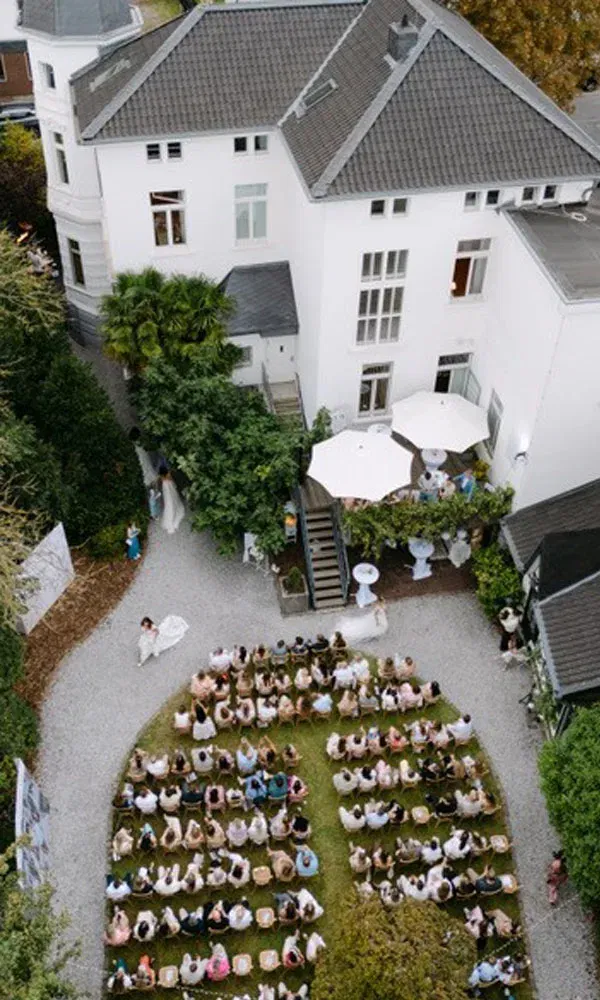 Gäste sitzen im Garten der Villa Lindström am Niederrhein in Halbkreis-Formation und verfolgen die Modenschau zur Eröffnung des Flagship-Stores.