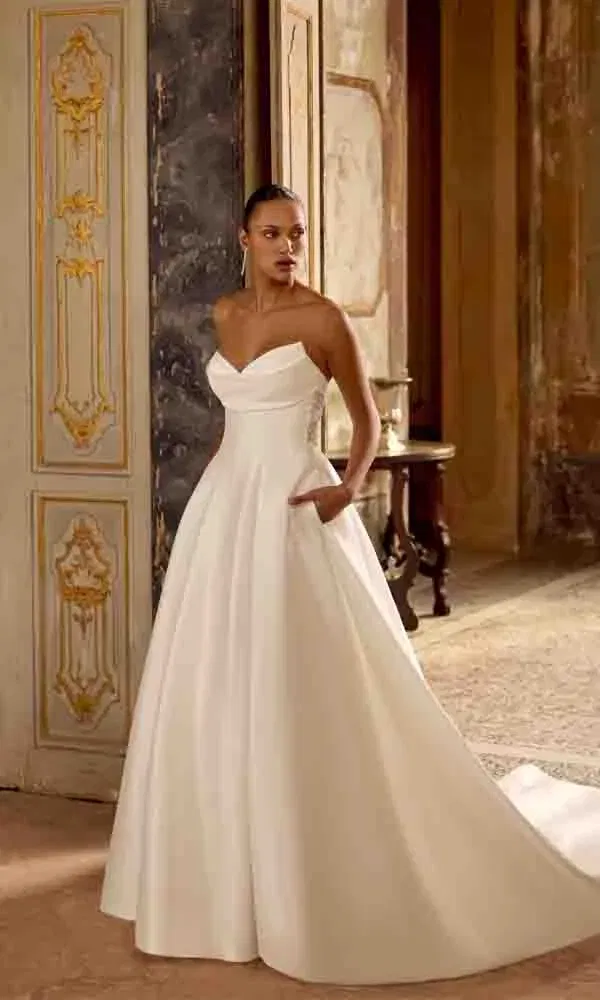 Moderne Braut in einem schulterfreien Satin-Kleid mit eleganter Schleppe und praktischen Seitentaschen.