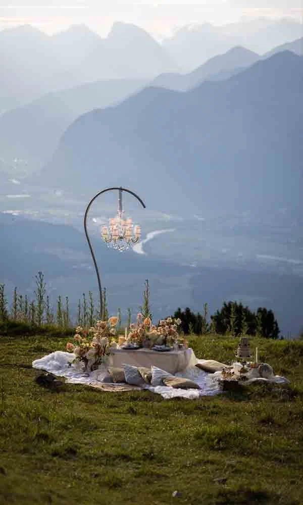 Romantische Outdoor-Szene mit gedecktem Tisch, Blumenschmuck und Bergpanorama.