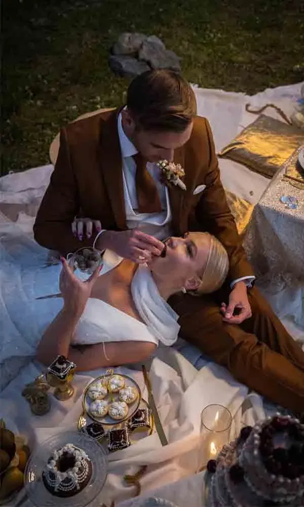 Intimer Moment: Braut liegt im Arm des Bräutigams und probiert Pralinen beim Luxus-Picknick.