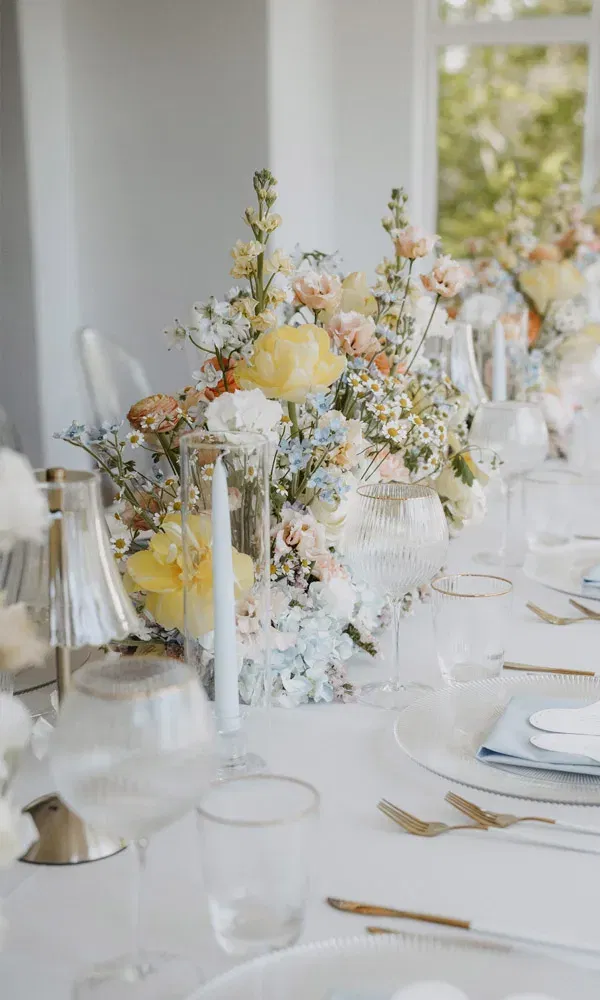 Festlich gedeckter Hochzeitstisch mit eleganten Gläsern, goldenen Details und üppiger Blumendekoration in Pastelltönen.
