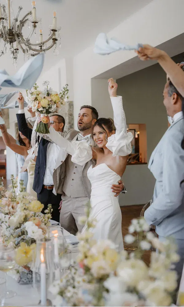 Fröhlicher Moment bei der Hochzeitsfeier: Braut und Bräutigam jubeln gemeinsam mit Gästen, während Servietten geschwungen werden.