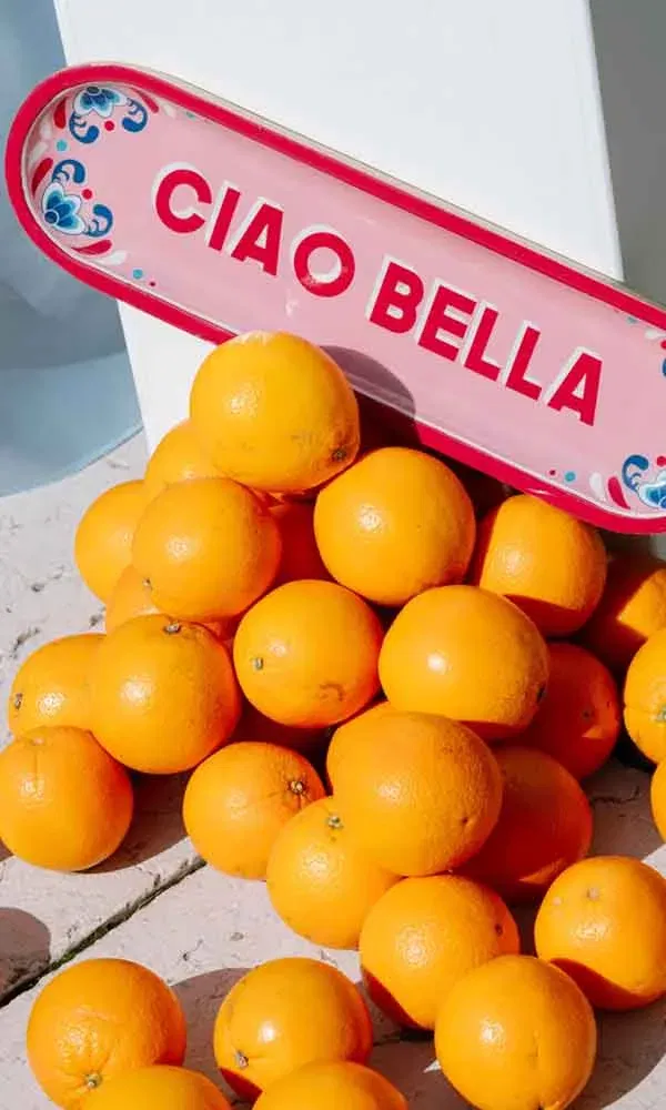 Dekoratives „Ciao Bella“-Schild mit frischen Orangen als fröhliches Detail einer mediterranen Sommerhochzeit.