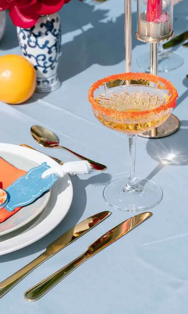 Elegant gedeckter Hochzeitstisch mit goldfarbenem Besteck, blauem Tischtuch und Cocktailglas mit farbigem Zuckerrand.