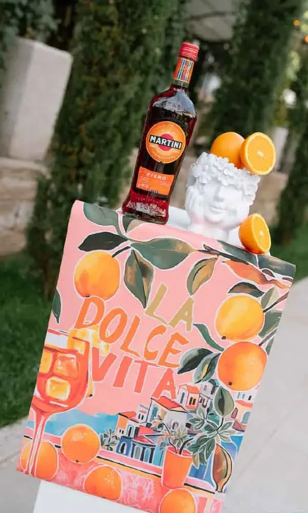 Dekoration mit „La Dolce Vita“-Schild, Orangen und Martini-Flasche als mediterranes Hochzeitsdetail.