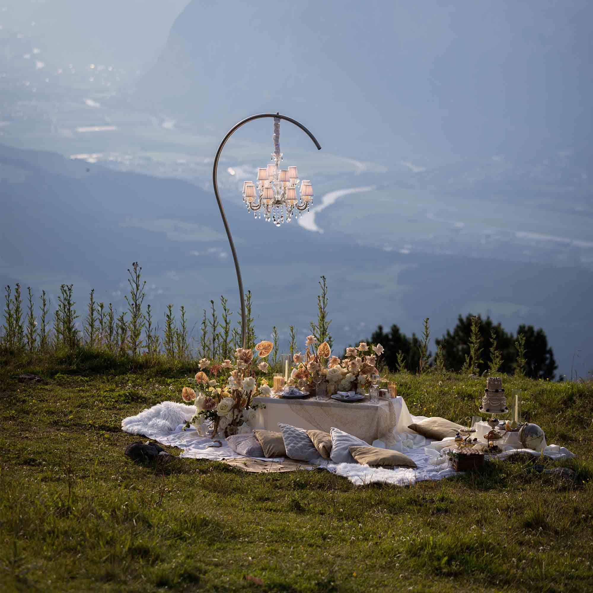 Stilvolles Hochzeitspicknick in den Bergen: dekorierte Tafel mit Blumen, Kerzen und Panoramablick ins Tal.