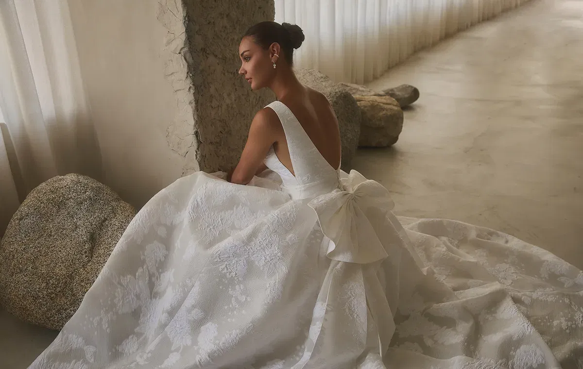 Modernes Casablanca Hochzeitskleid mit tiefem Rückendekolleté, floraler Struktur und markanter Schleife.
