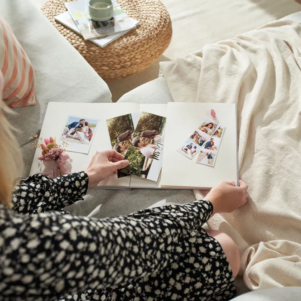 Eine Person blättert in einem Hochzeits-Fotobuch mit Bildern eines Paares am Strand, dekoriert mit floralen Elementen und der Aufschrift „Love“.