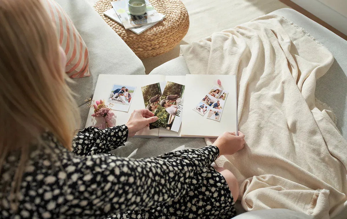 Eine Person blättert in einem Hochzeits-Fotobuch mit Bildern eines Paares am Strand, dekoriert mit floralen Elementen und der Aufschrift „Love“.