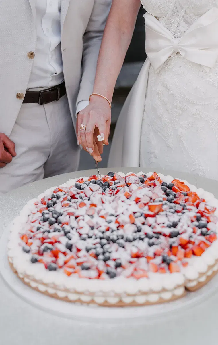 Hochzeitstorte mit Beeren und Sahne wird feierlich vom Paar angeschnitten.