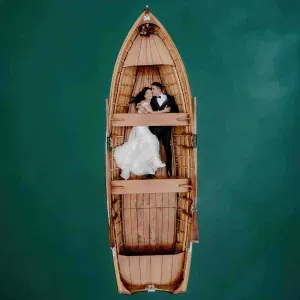 Romantisches Brautpaar liegt eng umschlungen in einem Holzboot auf türkisgrünem Wasser – aufgenommen aus der Vogelperspektive.