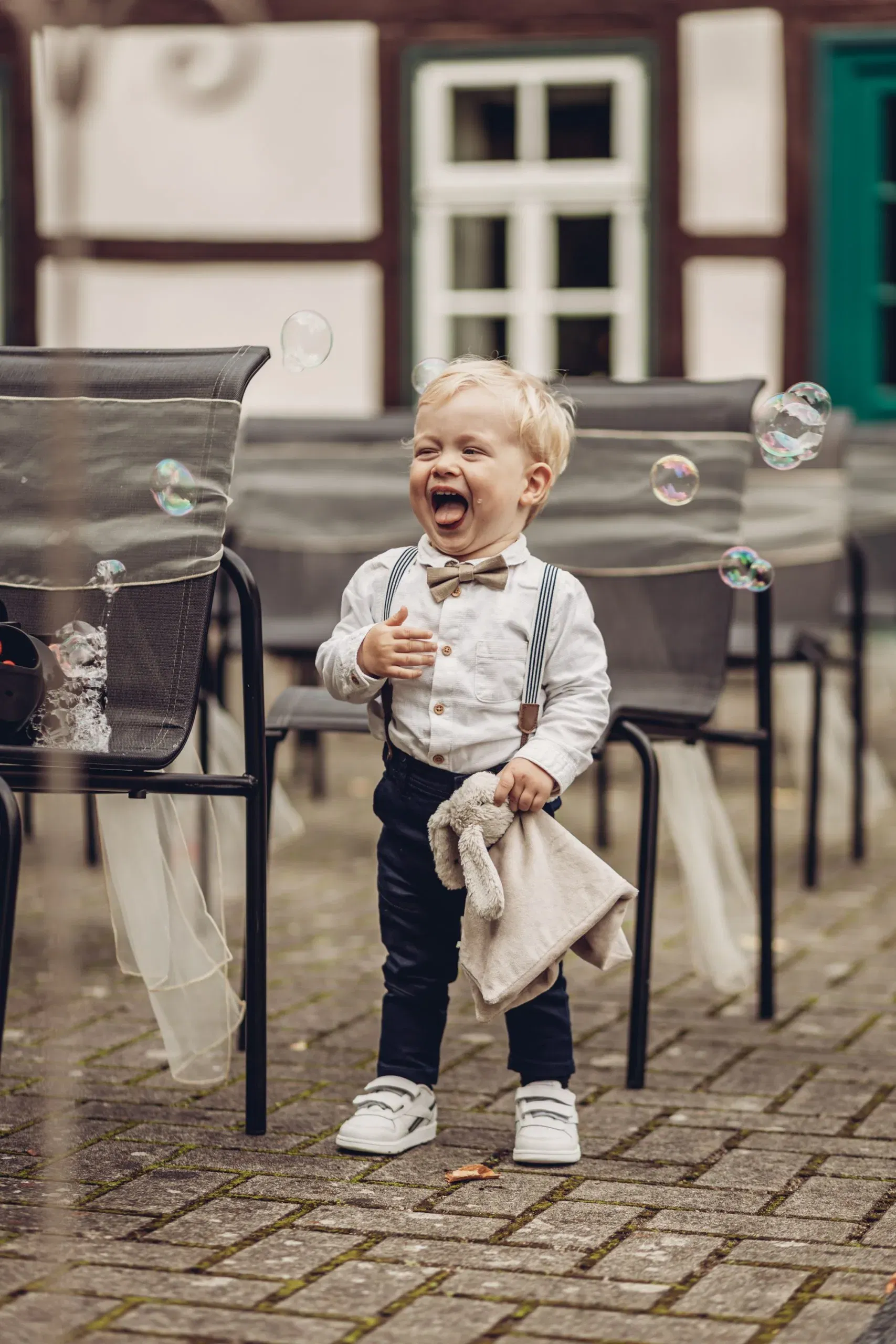 Lachender kleiner Junge in festlicher Kleidung spielt begeistert mit Seifenblasen – ein fröhlicher Moment während der Hochzeitsfeier.
