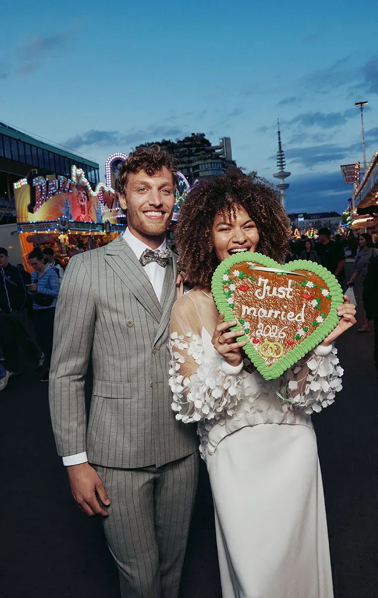 ein Hochzeitspaar auf einer Kirmes, die Braut beißt in ein Lebkuchenherz