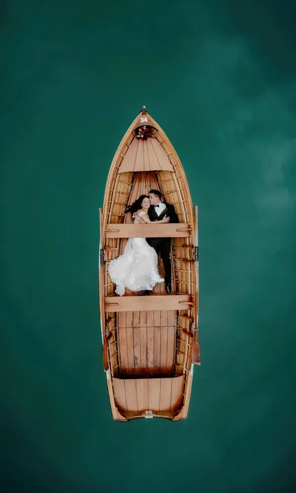Romantisches Brautpaar liegt eng umschlungen in einem Holzboot auf türkisgrünem Wasser – aufgenommen aus der Vogelperspektive.