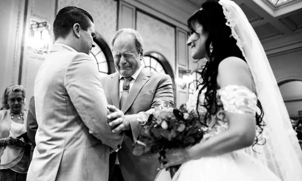 Emotionaler Moment während der Trauung: Der Vater der Braut übergibt seine Tochter sichtlich gerührt dem Bräutigam – festgehalten in berührender Schwarz-Weiß-Fotografie.