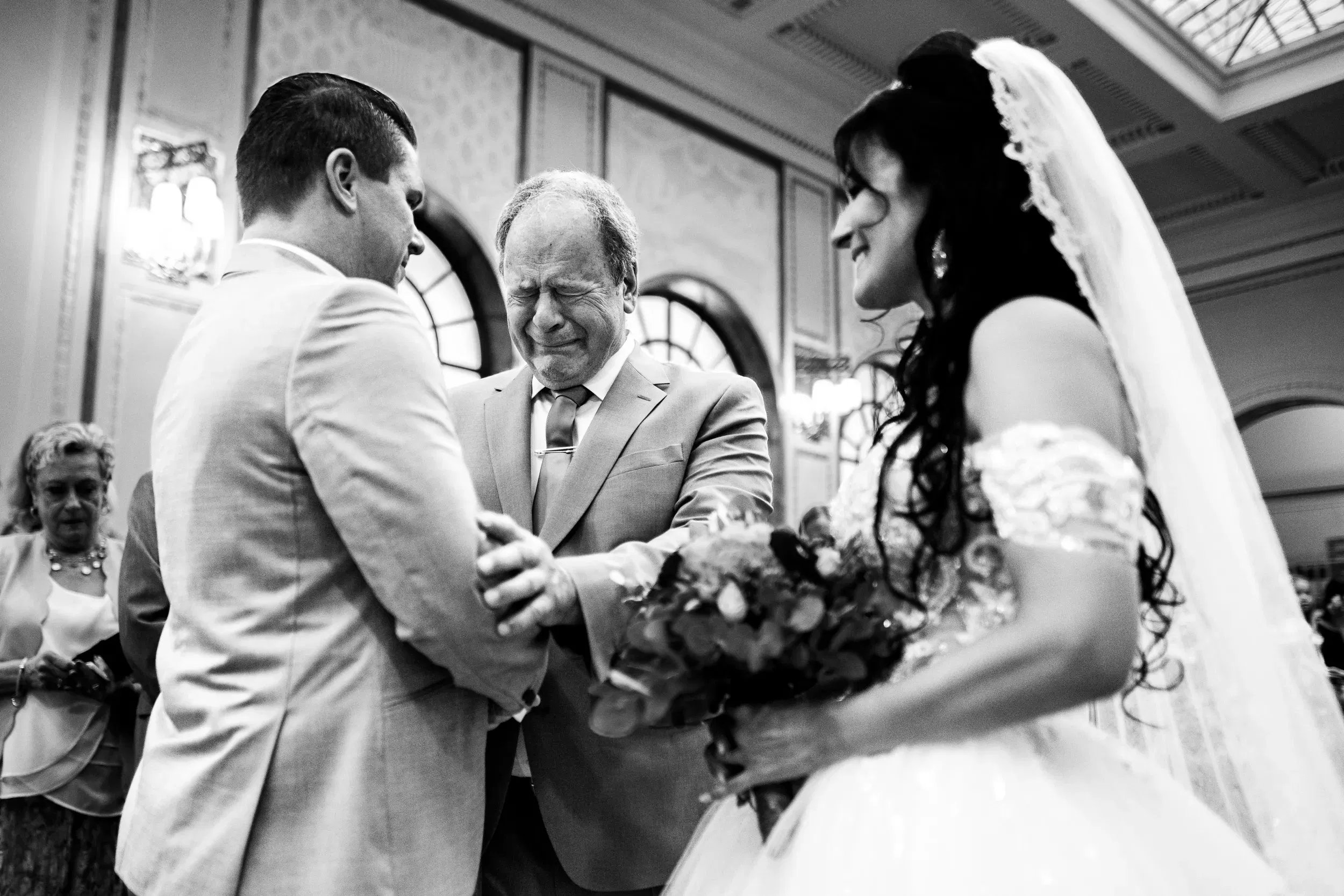 Emotionaler Moment während der Trauung: Der Vater der Braut übergibt seine Tochter sichtlich gerührt dem Bräutigam – festgehalten in berührender Schwarz-Weiß-Fotografie.