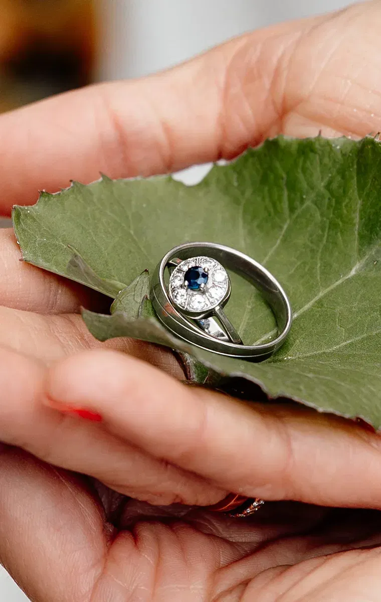 Zwei silberne Trauringe mit blauem Edelstein liegen auf einem grünen Blatt – Symbol einer Nature Wedding.