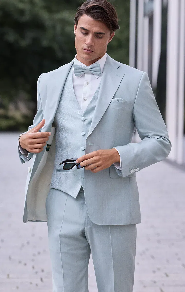 Bräutigam im mintfarbenen Anzug mit gemusterter Weste und Fliege – frischer Look mit sommerlicher Eleganz.