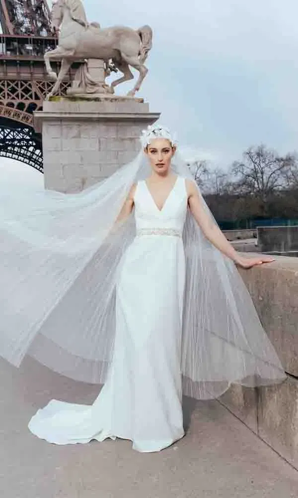 Elegante Braut in schlichtem weißen Kleid mit tiefem V-Ausschnitt und langem Schleier vor dem Eiffelturm.