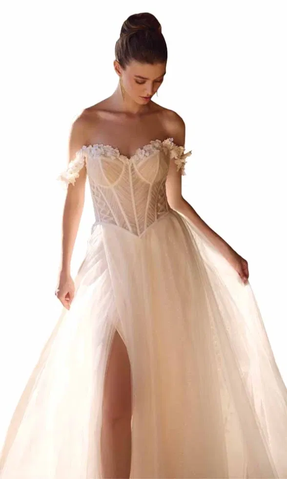 Brautmodell trägt ein romantisches Brautkleid mit transparentem Korsagenoberteil, schulterfreien Ärmeln mit floralen Applikationen und fließendem Tüllrock mit Beinschlitz, hell inszeniert vor weißem Hintergrund.