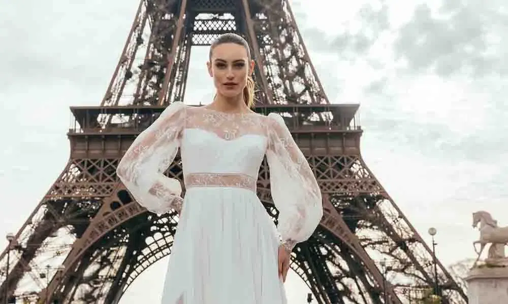 Selbstbewusste Braut in modernem Spitzenkleid mit langen Puffärmeln posiert vor dem Eiffelturm in Paris.