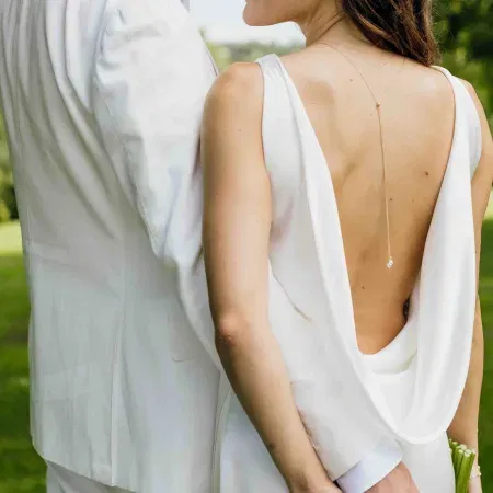 Braut in weißem Kleid mit tiefem Rückenausschnitt und feiner Rückenkette, während sie eng neben ihrem Partner steht.
