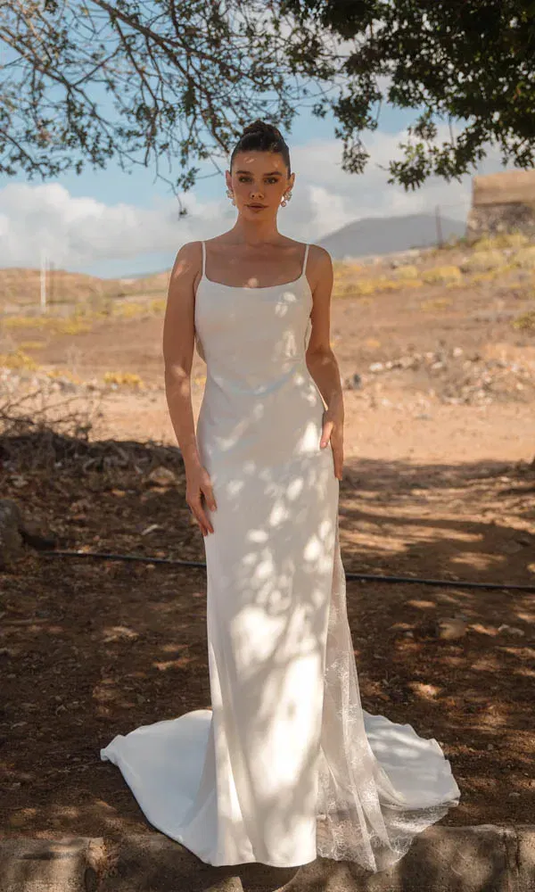 Schlichtes Brautkleid mit dünnen Trägern und zarter Schleppe, fotografiert im sonnigen Outdoor-Setting.