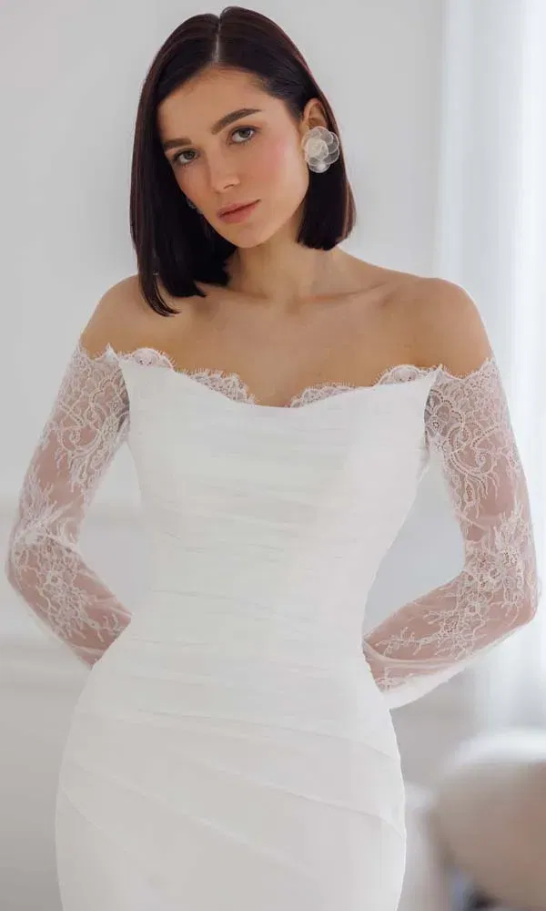 Elegantes Off-Shoulder-Brautkleid mit zarten Spitzenärmeln und drapiertem Oberteil in hellem Interieur.