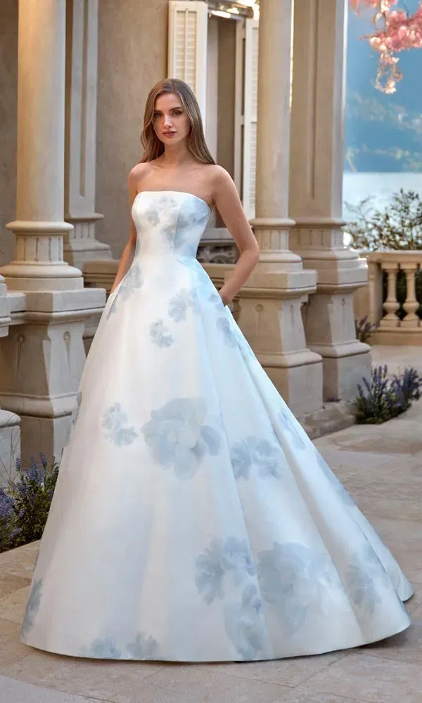 Elegantes A-Linien-Brautkleid mit zartblauen Blumenprints und schulterfreiem Mieder, fotografiert vor klassischer Architektur.