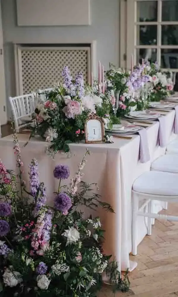 Aufwendig dekorierte Hochzeitstafel mit üppigen Blumenarrangements in Rosa, Weiß und Flieder sowie eleganten Kerzen und einer Tischkarte mit der Nummer 1.
