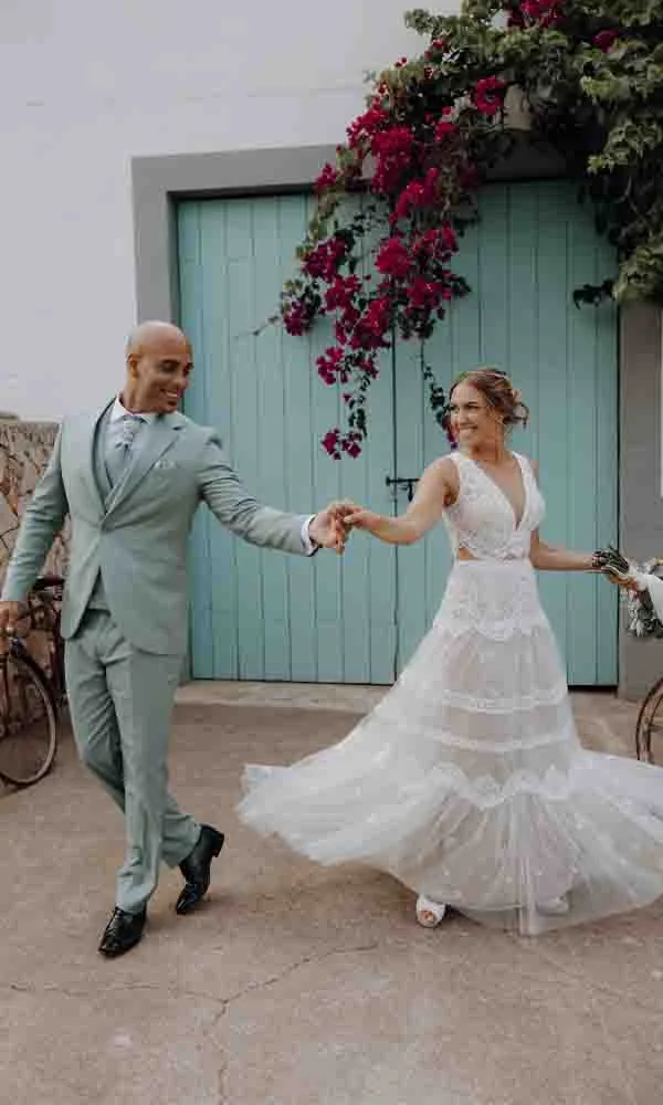 Brautpaar tanzt fröhlich vor einer mintgrünen Tür, die Braut in einem luftigen Spitzenkleid, der Bräutigam im pastellgrünen Anzug.