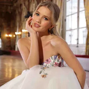 Braut im bestickten Kleid mit floralen Details, die sanft in die Kamera lächelt.