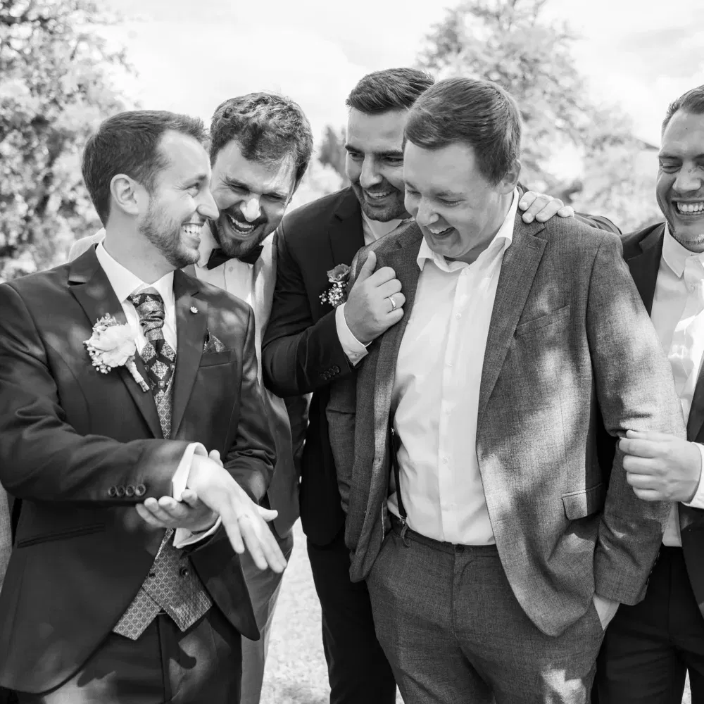 Der Bräutigam zeigt lachend seinen Ehering, während seine Freunde ausgelassen um ihn herumstehen.