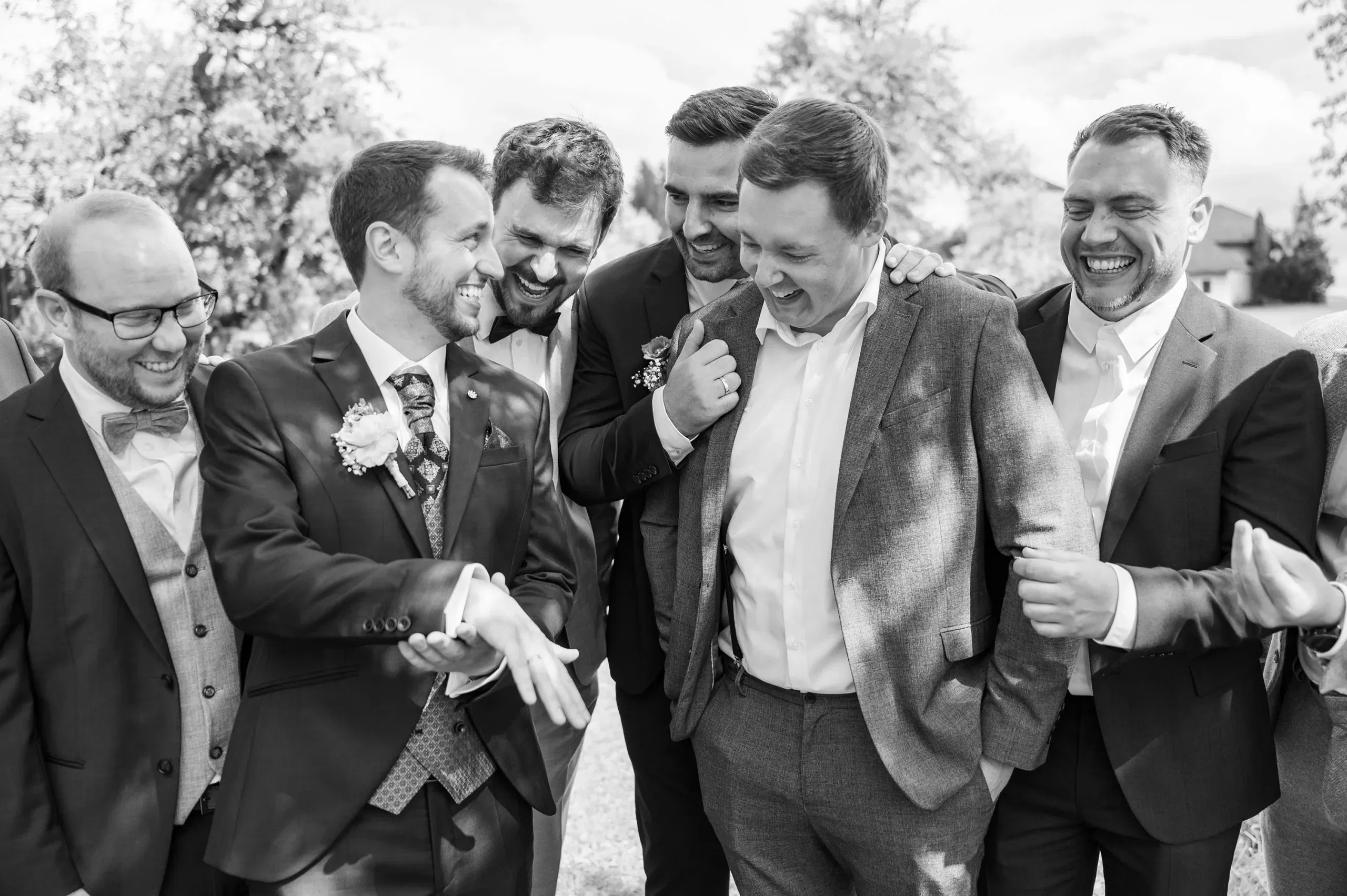 Der Bräutigam zeigt lachend seinen Ehering, während seine Freunde ausgelassen um ihn herumstehen.