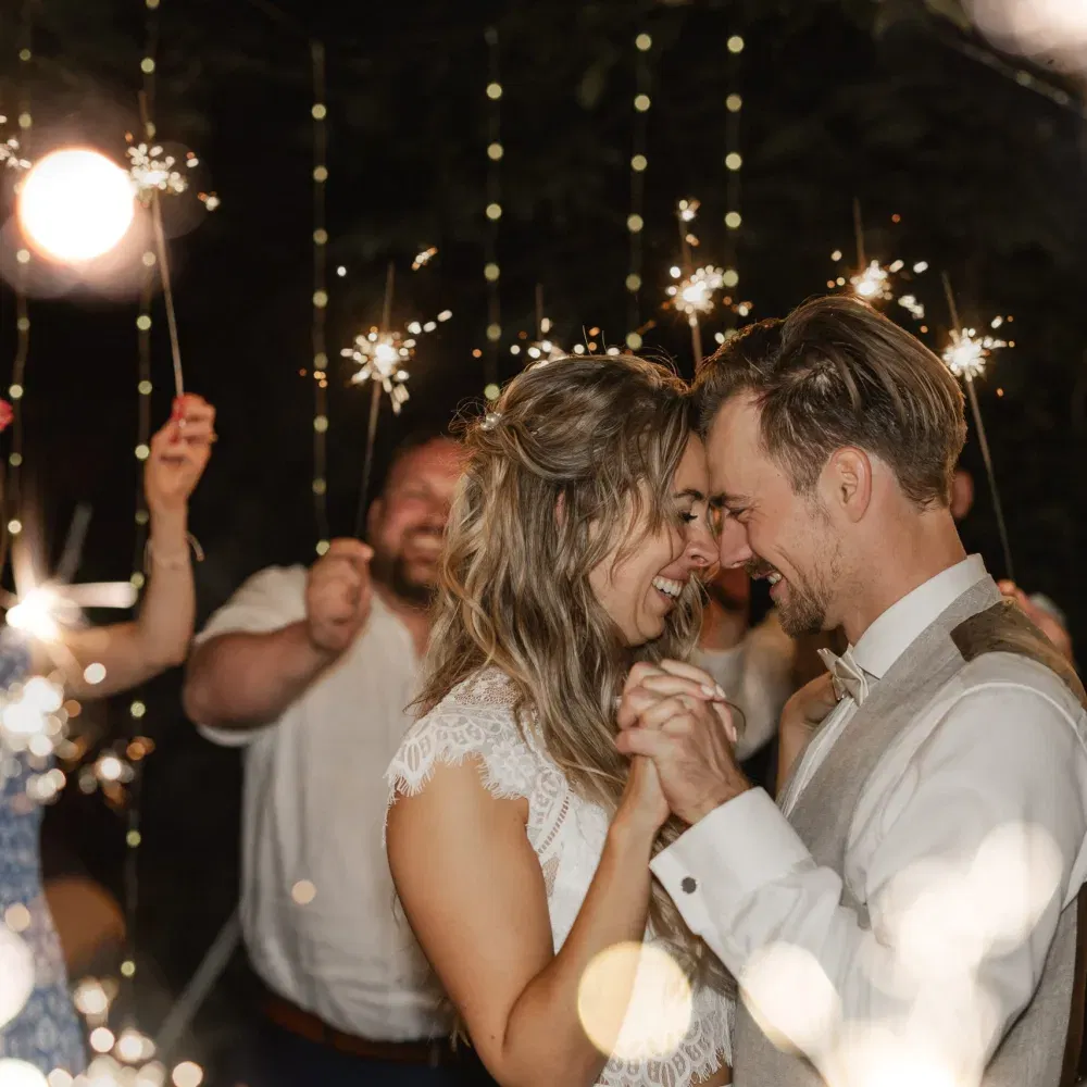 Braut und Bräutigam tanzen glücklich unter funkelnden Wunderkerzen, umgeben von ihren Gästen.