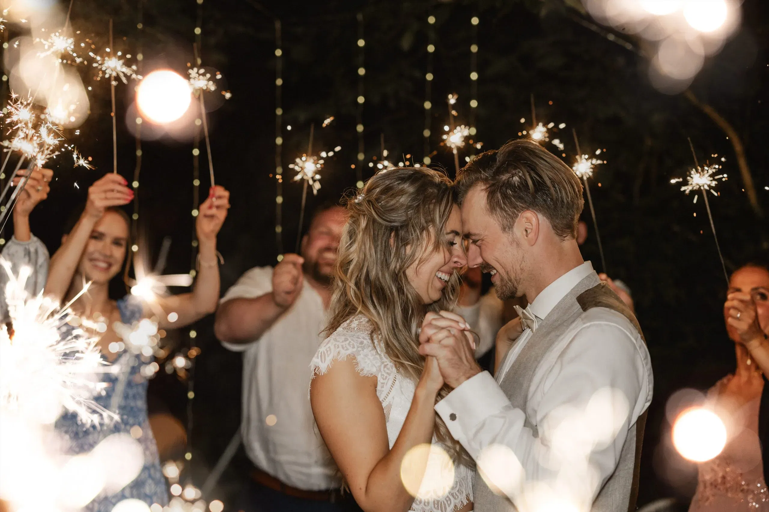 Braut und Bräutigam tanzen glücklich unter funkelnden Wunderkerzen, umgeben von ihren Gästen.