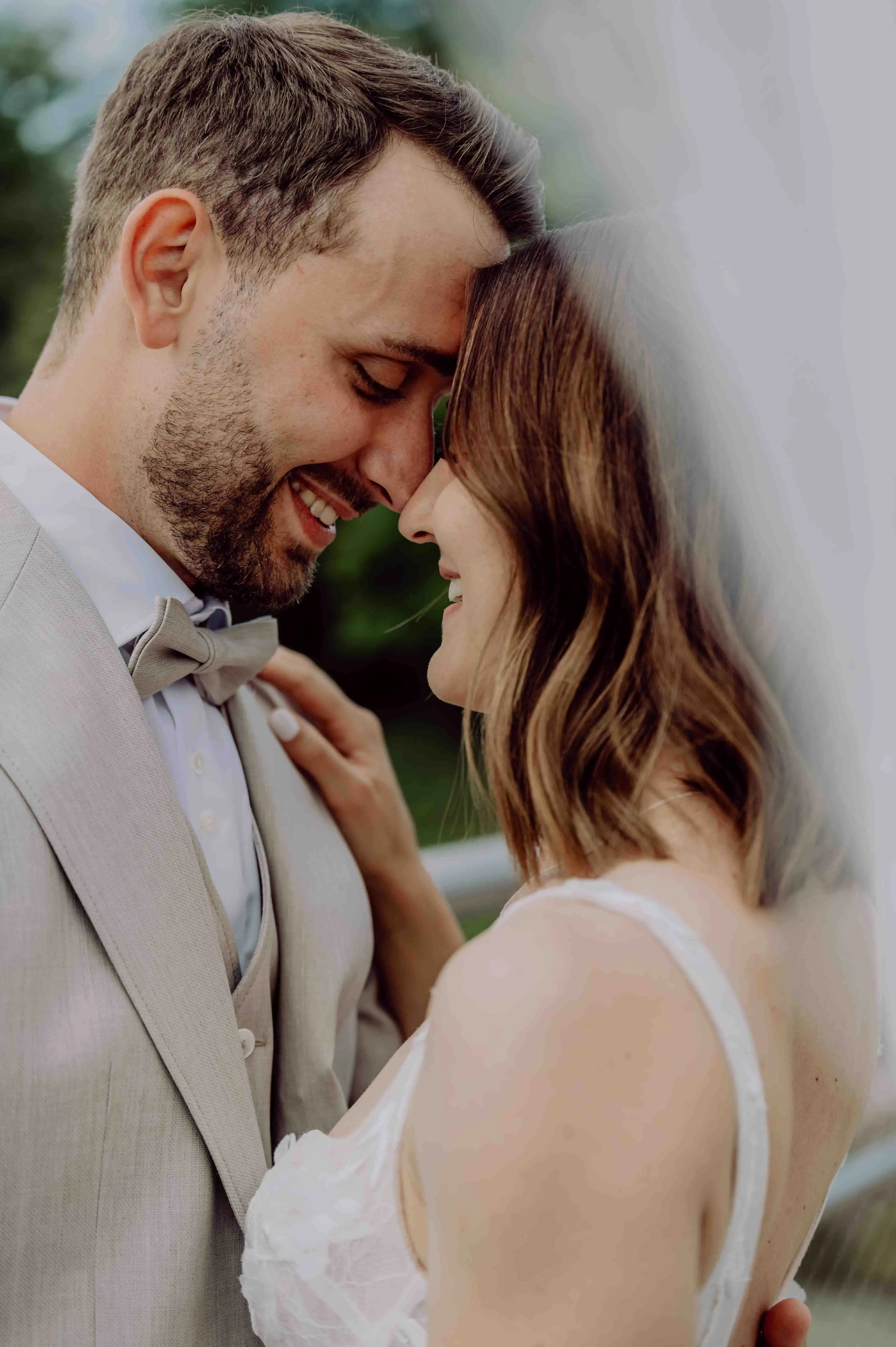 Braut und Bräutigam stehen Stirn an Stirn, lächeln liebevoll und genießen einen zarten Moment der Nähe.