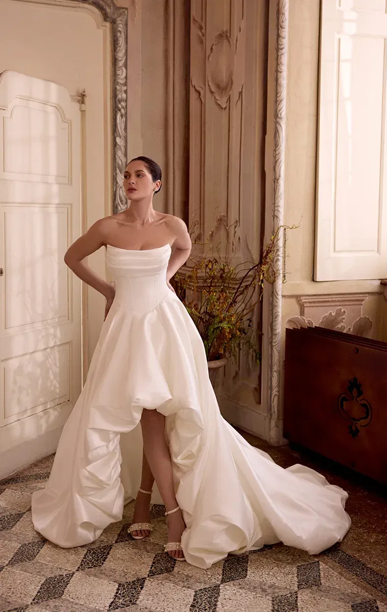 Strapless-Brautkleid mit voluminösem High-Low-Rock und langer Schleppe, getragen in einem kunstvoll verzierten Interieur
